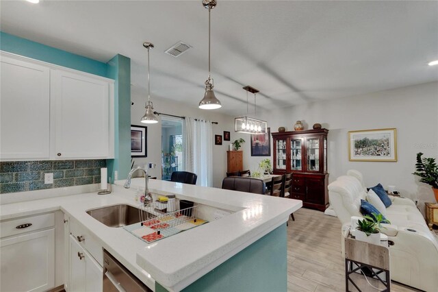 kitchen featuring visible vents, a peninsula, a sink, stainless steel dishwasher, and open floor plan