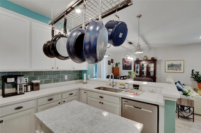 kitchen with a peninsula, a sink, decorative backsplash, stainless steel dishwasher, and open floor plan