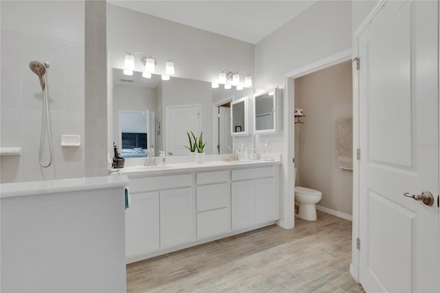 bathroom featuring double vanity, toilet, a walk in shower, and a sink