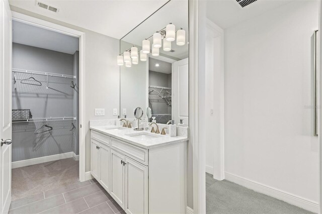 bathroom with baseboards, visible vents, double vanity, a sink, and a walk in closet