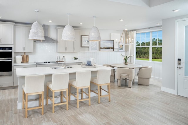 17420 Moonflower Dr Unit 101, Venice, FL 34293 - kitchen with black electric cooktop, light countertops, double oven, a sink, and wall chimney exhaust hood