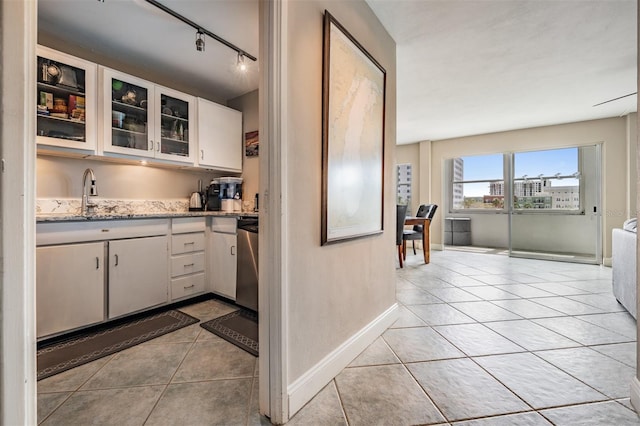 kitchen featuring light stone countertops, light tile patterned flooring, a sink, white cabinets, and stainless steel dishwasher
