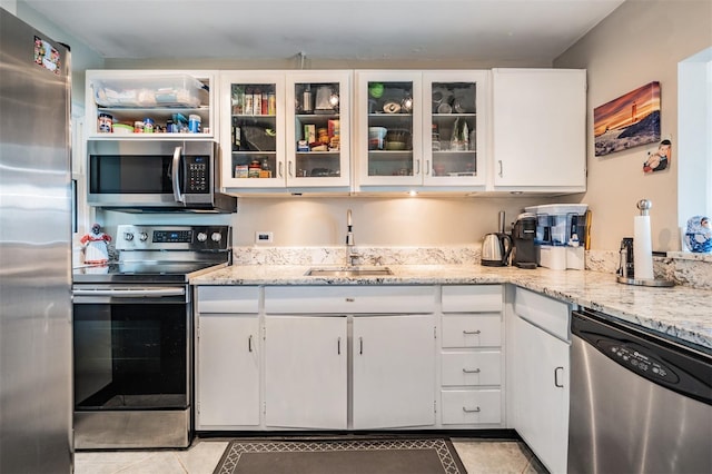 kitchen with light stone countertops, white cabinetry, stainless steel appliances, and a sink