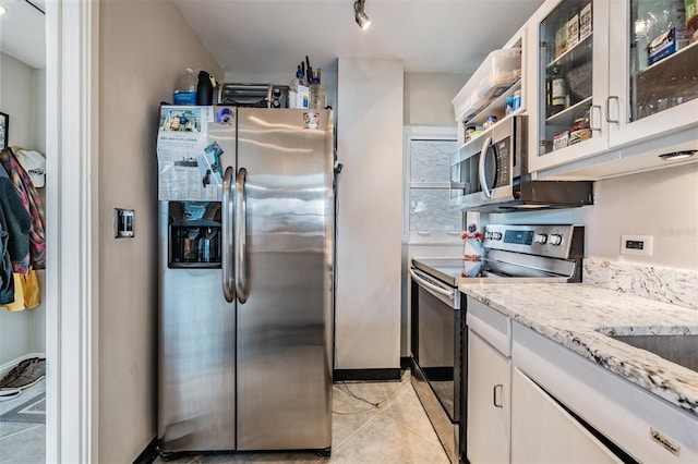 kitchen featuring light stone counters, stainless steel appliances, white cabinets, light tile patterned floors, and glass insert cabinets