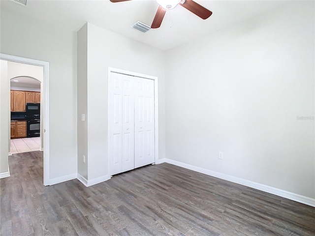 unfurnished bedroom featuring arched walkways, visible vents, baseboards, and dark wood-style flooring