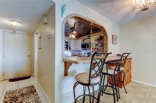 kitchen featuring tile countertops, arched walkways, appliances with stainless steel finishes, and a textured ceiling