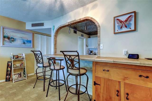 kitchen with baseboards, visible vents, tile counters, a textured ceiling, and brown cabinets