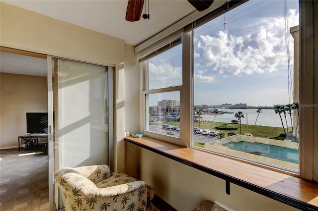 sunroom with a ceiling fan and a water view