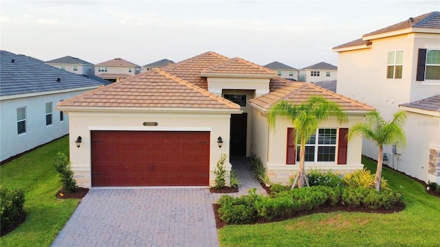 mediterranean / spanish-style home with stucco siding, a tile roof, decorative driveway, a front yard, and a garage