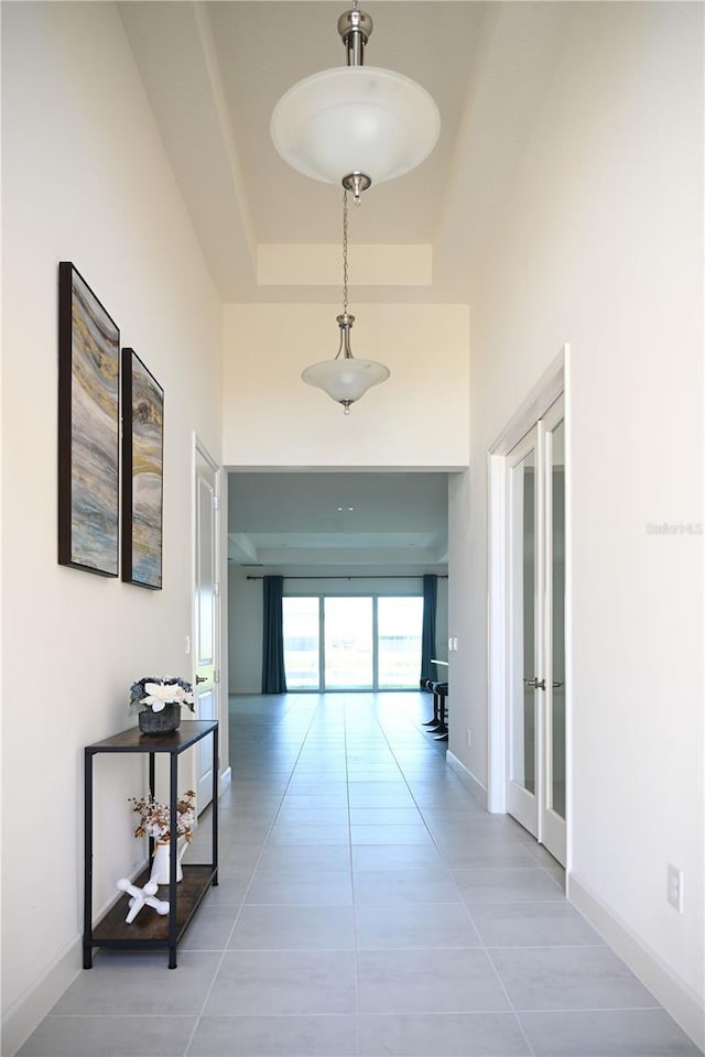 hall featuring tile patterned floors, a high ceiling, a raised ceiling, and baseboards