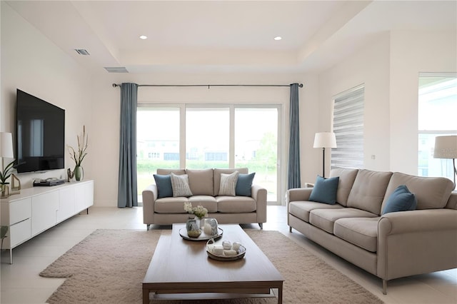 living area with a tray ceiling, visible vents, and light tile patterned flooring