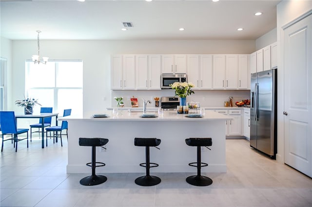 kitchen with a breakfast bar area, visible vents, stainless steel appliances, light countertops, and white cabinetry