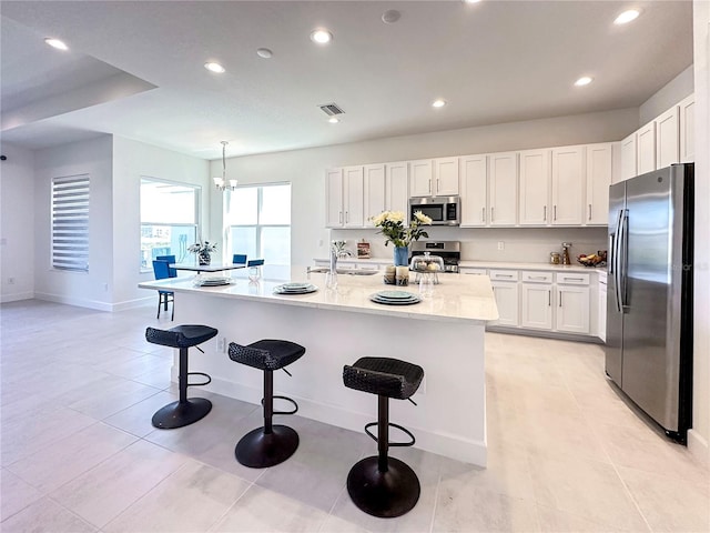 kitchen featuring visible vents, a breakfast bar area, appliances with stainless steel finishes, white cabinets, and a sink