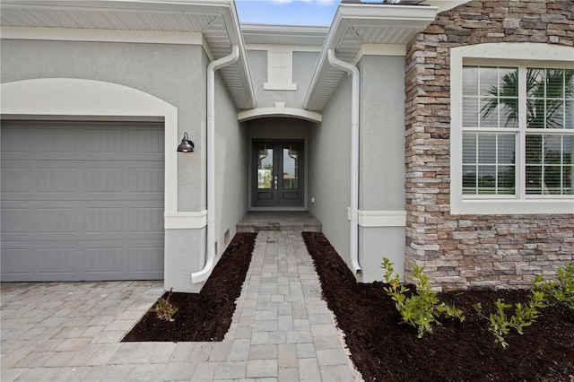 doorway to property featuring stone siding, stucco siding, an attached garage, and french doors