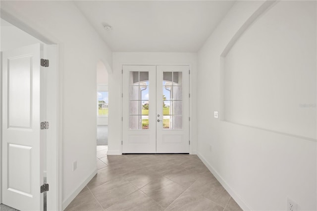 doorway featuring light tile patterned floors, french doors, arched walkways, and baseboards