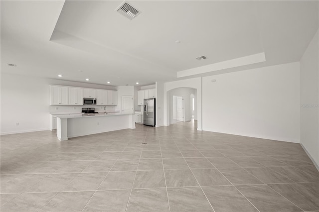 unfurnished living room with arched walkways, visible vents, a tray ceiling, and a sink