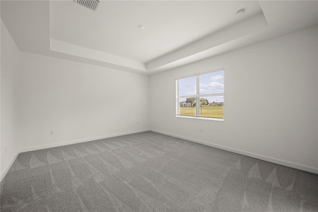 unfurnished room with visible vents, a raised ceiling, baseboards, and carpet flooring