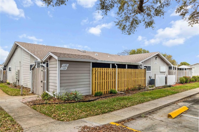 view of home's exterior with roof with shingles and fence