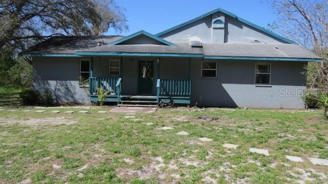 view of front of house with stucco siding, covered porch, and a front yard