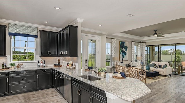 kitchen with dark cabinetry, a peninsula, a sink, stainless steel dishwasher, and open floor plan