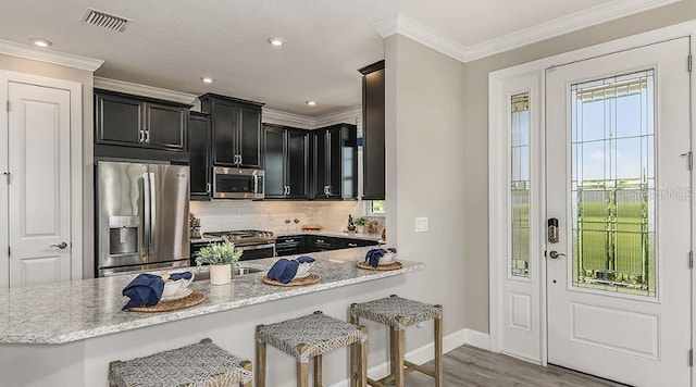 kitchen with light stone countertops, visible vents, appliances with stainless steel finishes, crown molding, and dark cabinets