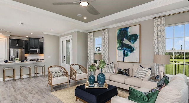 living room with a ceiling fan, visible vents, light wood finished floors, crown molding, and a raised ceiling