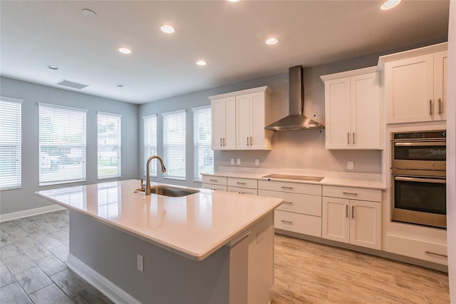 324 37th Ave NE, Saint Petersburg, FL 33704 - kitchen with a kitchen island with sink, double oven, wall chimney range hood, a sink, and light wood finished floors