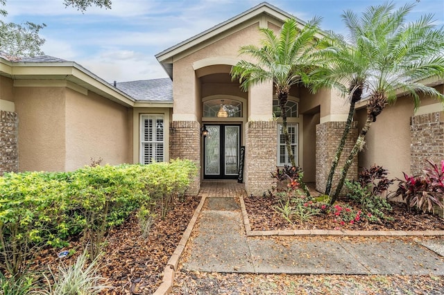 doorway to property featuring brick siding, stucco siding, and french doors