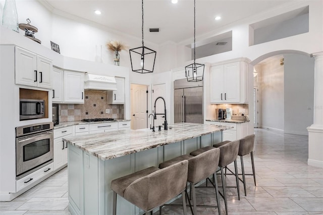 kitchen with premium range hood, arched walkways, appliances with stainless steel finishes, crown molding, and marble finish floor