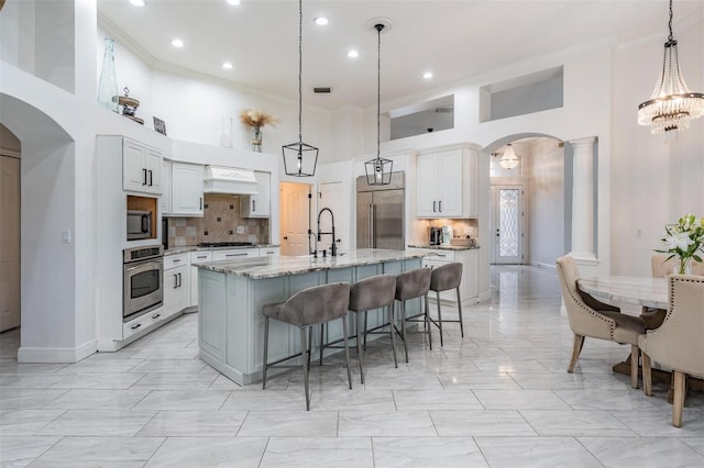 kitchen with crown molding, premium range hood, arched walkways, stainless steel appliances, and ornate columns