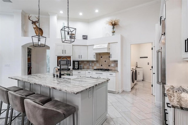 kitchen with a breakfast bar, arched walkways, custom range hood, appliances with stainless steel finishes, and washer and clothes dryer