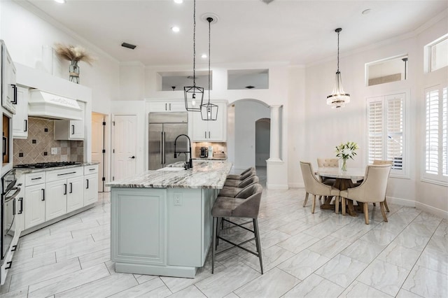 kitchen with custom exhaust hood, arched walkways, a sink, built in refrigerator, and crown molding