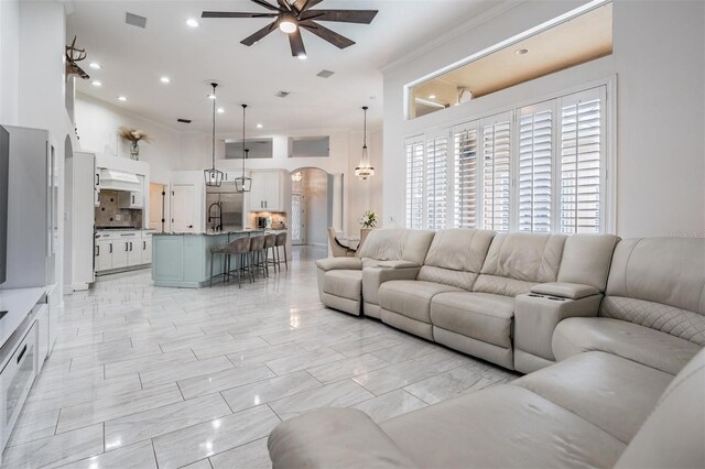 living room with visible vents, crown molding, ceiling fan, a towering ceiling, and arched walkways