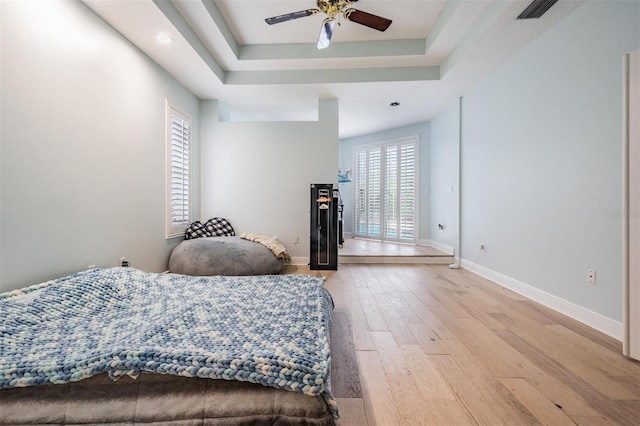 bedroom with visible vents, baseboards, light wood finished floors, a tray ceiling, and ceiling fan