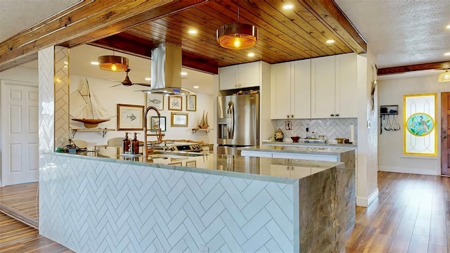 kitchen featuring island range hood, beamed ceiling, decorative backsplash, wood finished floors, and stainless steel fridge