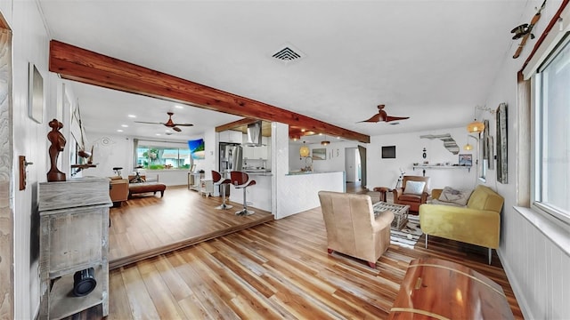 living room with hardwood / wood-style flooring, a ceiling fan, visible vents, and beam ceiling