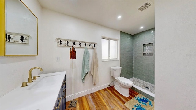 full bath with visible vents, toilet, wood finished floors, a tile shower, and vanity