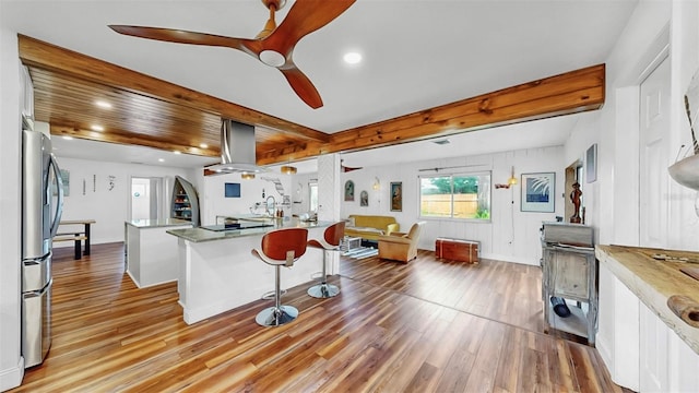 kitchen with light wood-type flooring, beam ceiling, freestanding refrigerator, island range hood, and ceiling fan