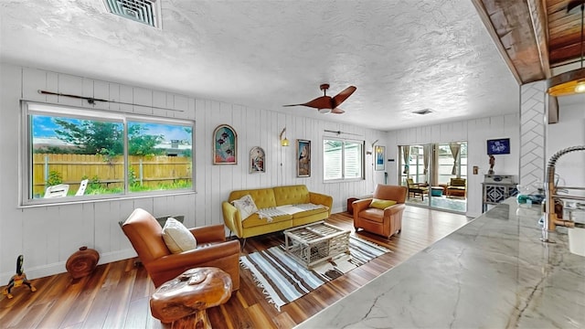 living area with visible vents, baseboards, a textured ceiling, and hardwood / wood-style flooring