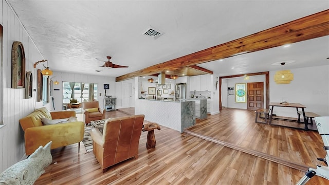 living area featuring light wood finished floors, visible vents, beamed ceiling, and a ceiling fan