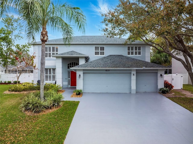 traditional-style house featuring an attached garage, fence, driveway, and stucco siding