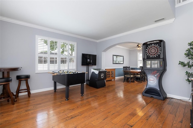 recreation room featuring visible vents, ornamental molding, hardwood / wood-style floors, arched walkways, and baseboards