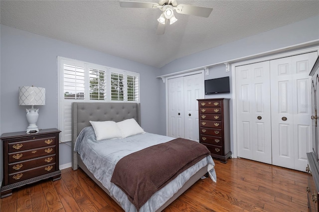 bedroom with multiple closets, a textured ceiling, wood finished floors, and vaulted ceiling