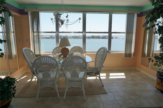 unfurnished dining area with tile patterned floors, baseboards, a water view, and an inviting chandelier