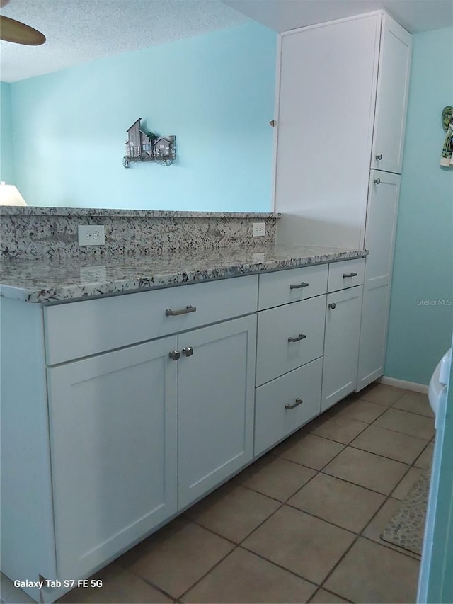 kitchen featuring light tile patterned floors, white cabinets, light stone countertops, and baseboards