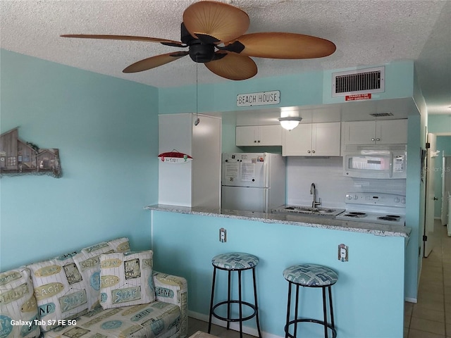 kitchen with white appliances, a sink, a textured ceiling, a breakfast bar, and tile patterned floors