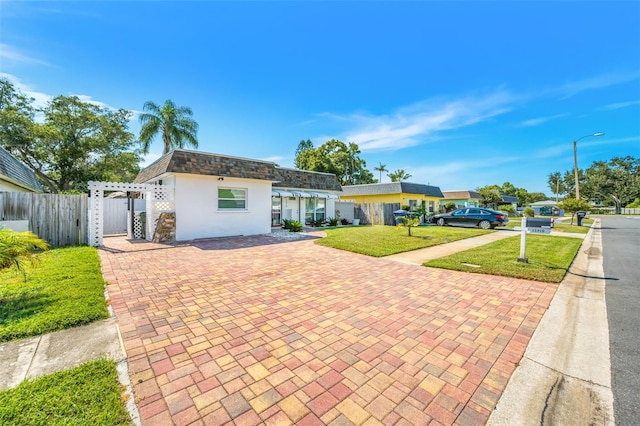 view of front of house featuring decorative driveway, a front yard, mansard roof, and fence