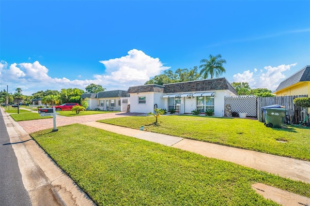 view of property with mansard roof, decorative driveway, fence, roof with shingles, and a front yard