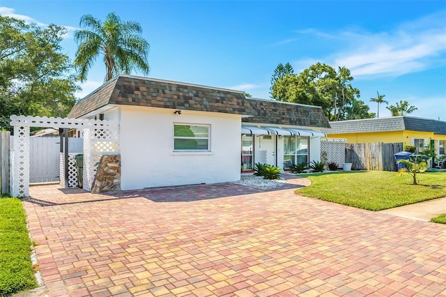 back of property with fence, mansard roof, a pergola, a shingled roof, and a lawn