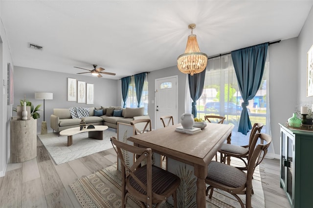 dining space featuring light wood-style flooring, ceiling fan with notable chandelier, and visible vents